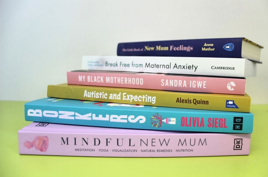 A pile of books on a yellow table. From top to bottom the titles are: New Mum Feelings, Break Free from Maternal Anxiety, My Black Motherhood, Autistics and Expecting, Bonkers and Mindful New Mum.