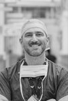 An image of Giangiacomo Ollandini in scrubs and surgical cap, wearing a face mask around his neck
