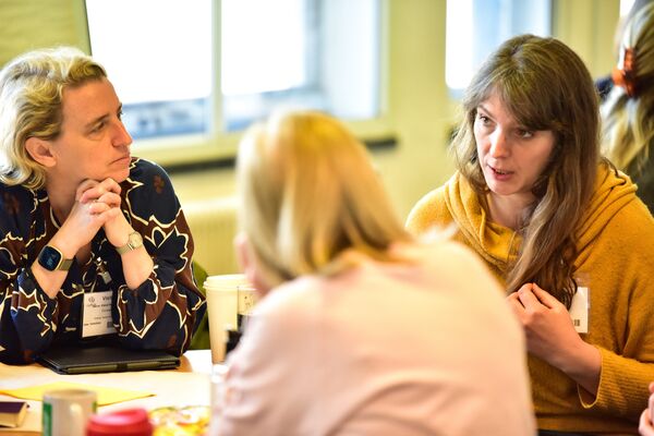 A photograph of three women sitting around a table talking.