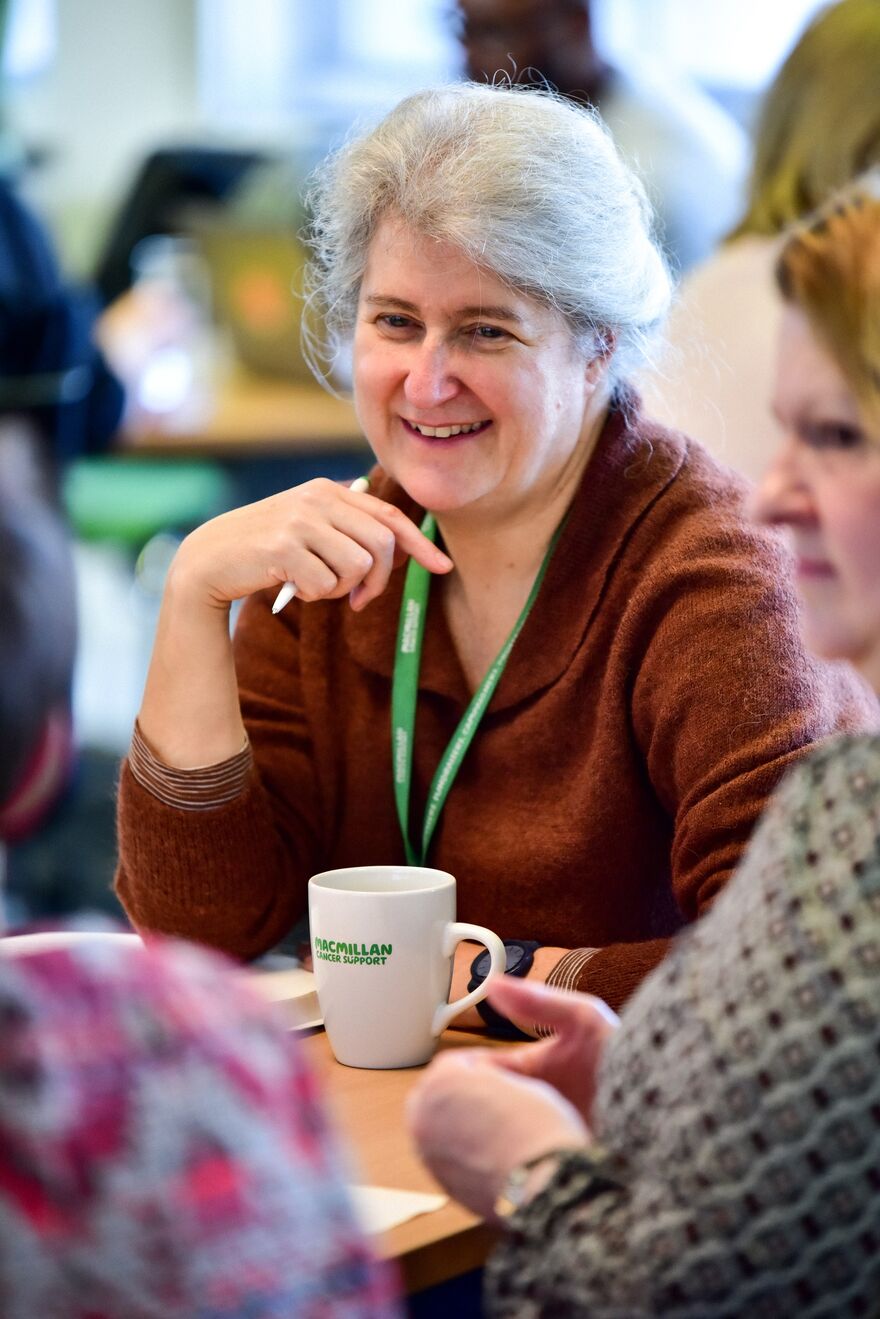 A group of PIF members sitting around a table. In the centre of the image is a woman wearing a brown jumper with a Macmillan lanyard.